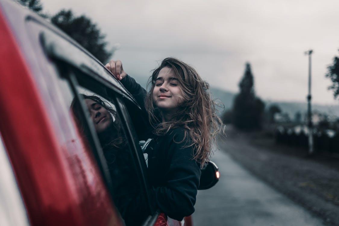 a woman leaning on a rolled down car window to feel the breeze during a car ride.